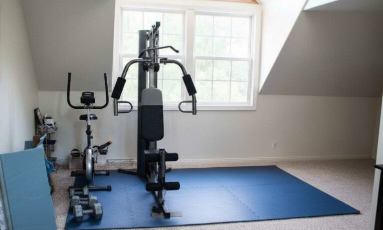 Kućna teretana sa sobnim biciklom, multifunkcionalnom spravom za tegove i tegovima na plavoj prostirci