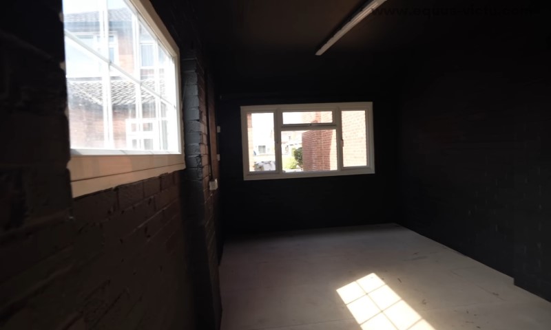 Slabo osvetljena, uska soba sa crnim zidovima i belim okvirima prozora