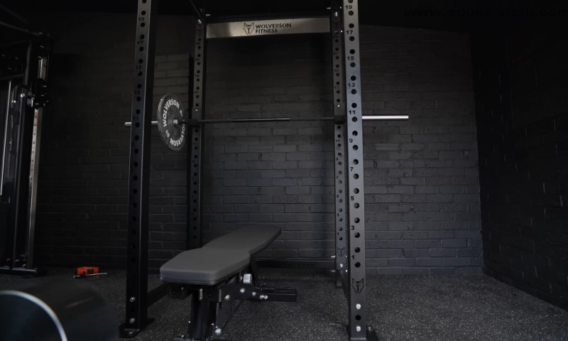 Slabo osvetljena teretana sa crnim zidom od cigle ima stalak za čučnjeve i klupski potisak