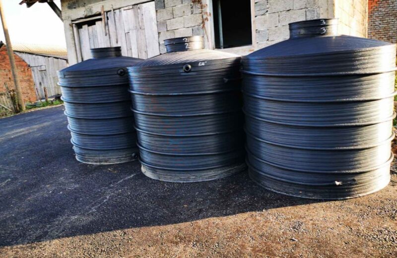 Tri velika crna plastična rezervoara za skladištenje vode postavljena pored pomoćnog objekta